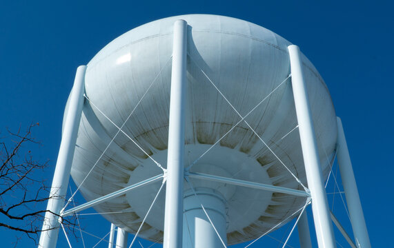 Iconic white elevated water tower against a brilliant clear blue sky, viewed from below, showcasing vital utility infrastructure and a symbol of municipal water supply in a town.