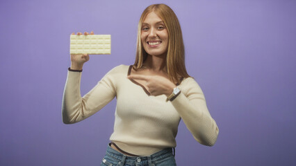Young woman holding white chocolate bar points finger toward camera in studio; playful product...