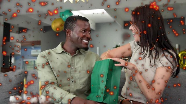 Couple sitting sofa partying, woman lifting green gift bag starting wood box reveal, overlay hiding