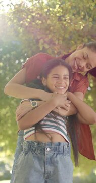 Pulling child close, mom behind daughter hugging, showing love under park tree, red tee, sun, watch
