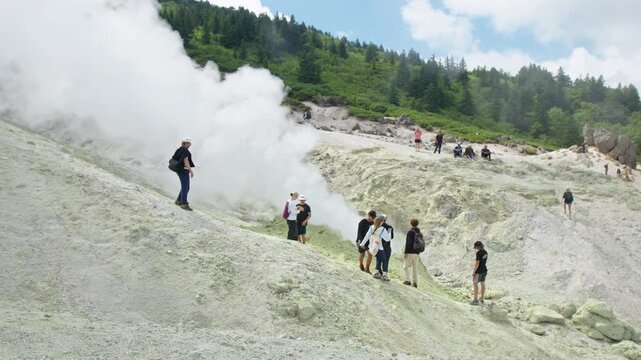 Group of hikers stand near the smoking fumarole on the active volcanic area on Kunashir Island in Russia