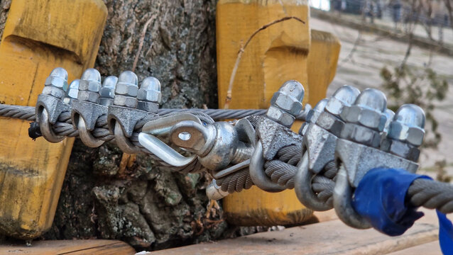 A steel cable fastening knot, fixed with metal clamps (U-shaped clamps). The cable forms a loop around a metal bushing, which is connected to a bracket or other element of the rigging. Rope park