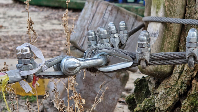 A steel cable fastening knot, fixed with metal clamps (U-shaped clamps). The cable forms a loop around a metal bushing, which is connected to a bracket or other element of the rigging. Rope park