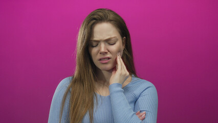 Fototapeta premium Young caucasian woman with pained expression hand on cheek in pink studio set; discomfort toothache.