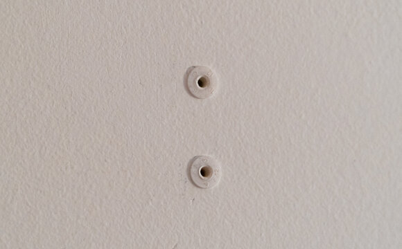 Close-up of two white plastic wall anchors embedded in a light beige, textured drywall surface, ideal for home improvement, mounting, and construction projects.