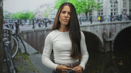 Fototapeta premium Woman adjusting belt and fingers near waist beside parked bicycle on a canal street bridge; quiet concern.