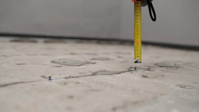 Close-up of a yellow tape measure on a rough concrete floor at a construction site.
