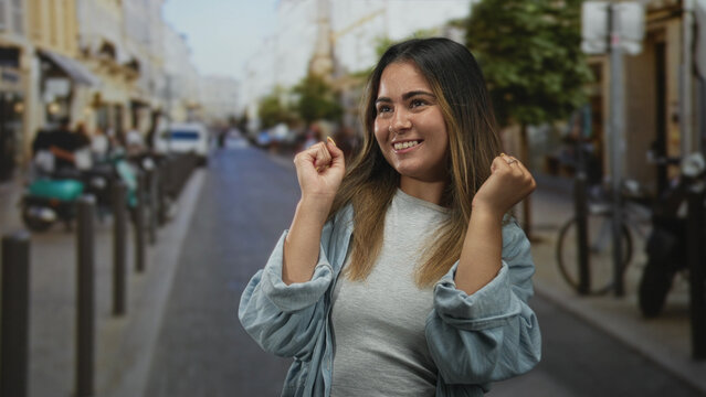Young woman holding hands to cheeks laughing on busy city street lined with scooters and bollards; joy.
