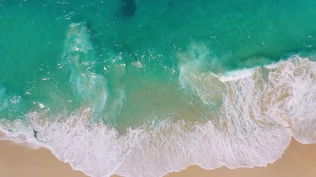 Aerial drone footage of massive turquoise waves crashing on a sandy tropical beach. Top view of powerful ocean surf and blue sea water. Concept of nature power, travel destination and summer.