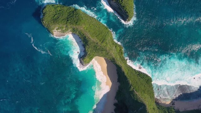 Aerial drone footage of Kelingking Beach in Nusa Penida, Indonesia. Massive turquoise waves crash on the sandy shore below the iconic T-Rex shaped cliff. Stunning view of the secluded cove.