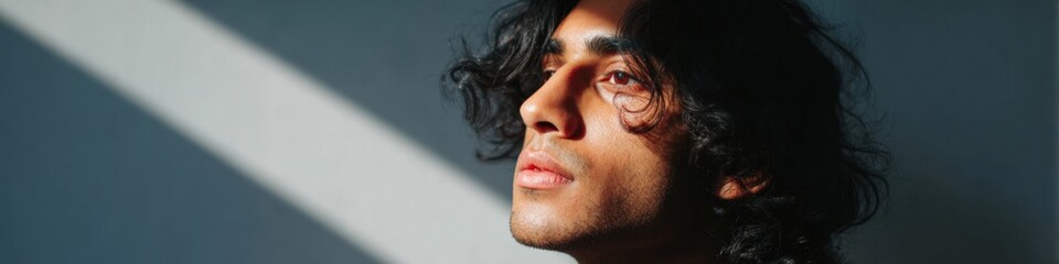 Obraz premium Male asian young adult closeup portrait dramatic sunlight stripe across face deep shadow moody expression curly black hair studio backdrop