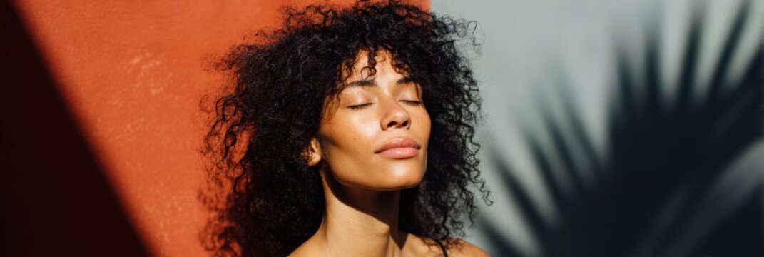 African female young sunlit portrait with curly hair eyes closed palm shadow on red and gray wall cinematic light