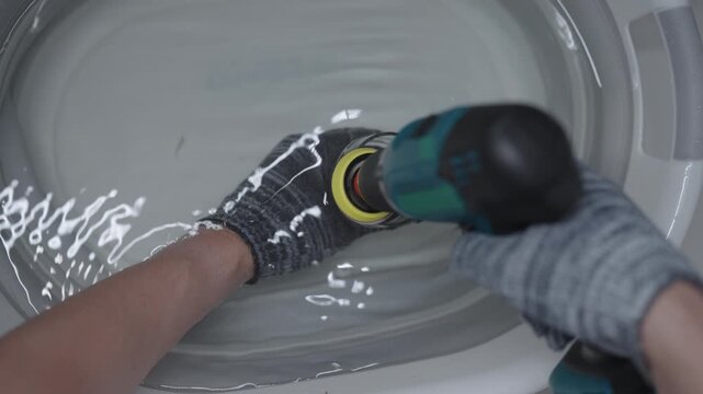 Person in protective gloves sanding cut glass bottle with orbital sander in water. Artisan grinding sharp edge of dark glass bottle to upcycle it. Transformation bottles into functional decor pieces.