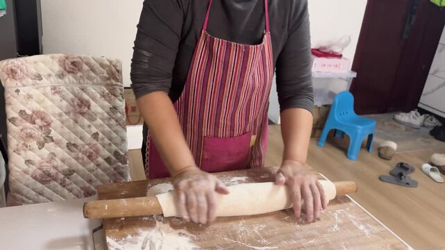 Preparing fresh noodles from scratch at home by shaping and cutting dough on a floured wooden board, showcasing traditional homemade cooking in a kitchen setting.