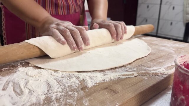 Preparing fresh noodles from scratch at home by shaping and cutting dough on a floured wooden board, showcasing traditional homemade cooking in a kitchen setting.