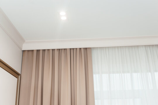 Beige curtain hanging on hidden ceiling cornice in modern bedroom. Textile drapery with sheer fabric for living room window decoration. Minimalist interior design and home renovation.
