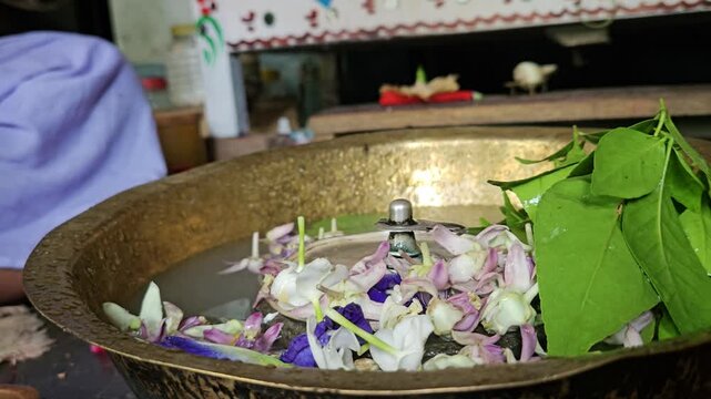 Shivling jal abhishek with flowers and bel leaves in Hindu temple, sacred water offering ritual to Lord Shiva, spiritual scene with devotion, tradition and religious culture in India