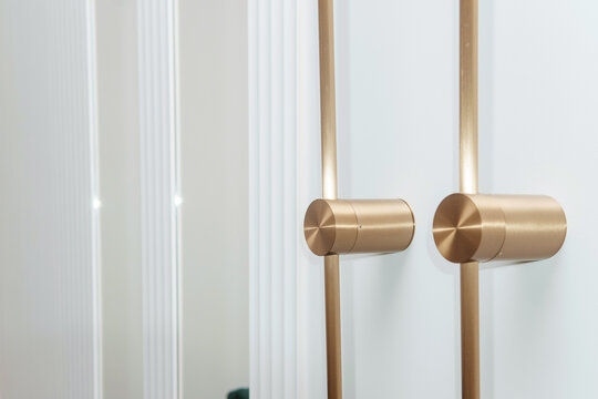 Modern gold door handle on white interior door. Minimalist metallic hardware detail for luxury home architecture. Contemporary room decor and stylish finishing touch for residential design.