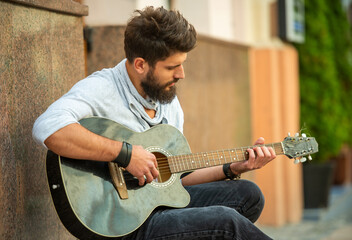Obraz premium Young man playing acoustic guitar outdoors, focused on music.