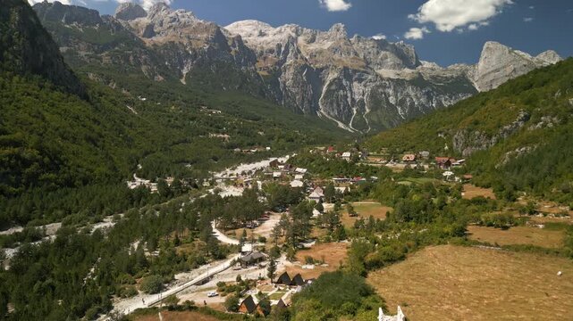 Aerial drone flying forward over Theth village in Albanian Alps, dramatic mountain peaks and lush valley landscape with traditional houses and scenic nature