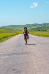 Fototapeta premium Woman walks down rural road under bright blue sky