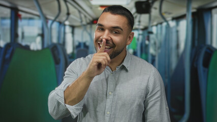 Young hispanic man standing upright on bus points finger to lips while making direct eye contact on street  secrecy caution privacy confidentiality. © Krakenimages.com