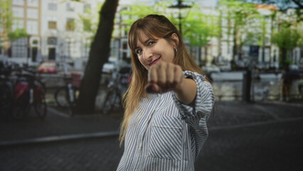 Woman with smiling face and hand near chest wearing striped shirt and hoop earrings on a street by a canal in amsterdam  confidence. © Krakenimages.com