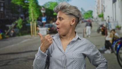 Fototapeta premium Woman in striped shirt pointing thumb on busy street lined with bicycles and parked cars; surprise.