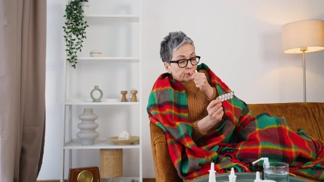 Sick elderly woman with cold symptoms taking medicine