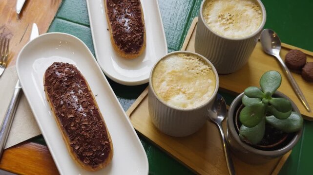 Fresh sweet eclairs cakes with cream cheese and chocolate chips with coffee on the table in a cozy cafe. High quality 4k footage