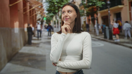 Fototapeta premium Woman finger to chin touching face on a street with blurred pedestrians and buildings; thoughtful confidence.