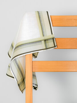 A classic cotton handkerchief with a green and grey plaid border draped elegantly over the back of a wooden chair.