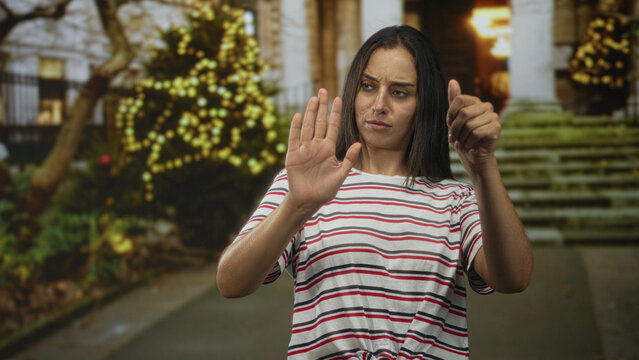 Woman holds hands forward miming steering on street with festive lights and stone steps; playful engagement.