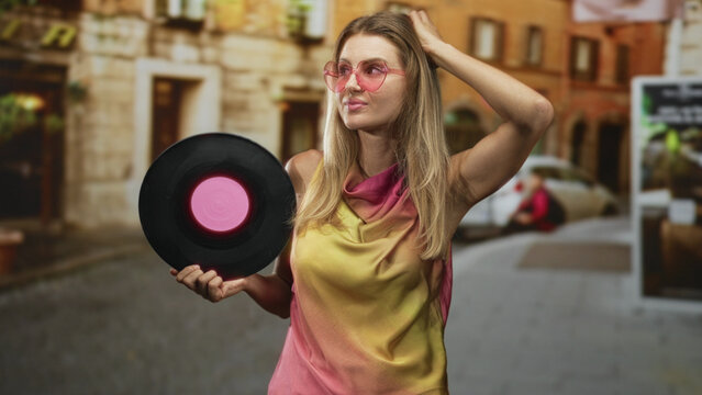 Woman holding vinyl record with hand on head and pink sunglasses on a cobbled street; nostalgia retro.
