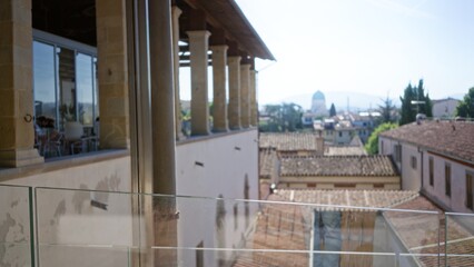 Fototapeta premium Sunlit terracotta rooftop view with distant dome, defocused balcony columns and glass railing, soft blurred skyline city; background backdrop copyspace calm.
