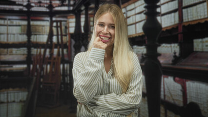 Woman blonde smiling with finger to chin and crossed arms amid tall bookshelves in library building  playful curiosity. © Krakenimages.com