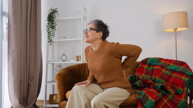 Senior woman experiencing sudden back pain sitting on a couch