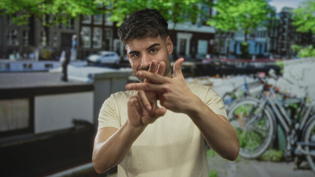 Young hispanic man uses interlaced fingers to form a hashtag sign on a busy city street; enthusiasm.