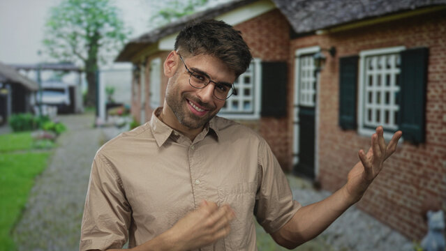 Young man casually uses hand to play air guitar gesture at building entrance on a sunny morning; imagination playfulness fun joy.