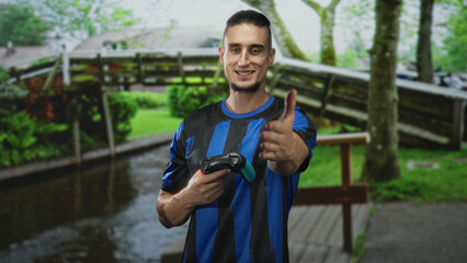 Man in blue striped shirt holding a gamepad and extending his right hand for a handshake in a forest  friendly sportsmanship. © Krakenimages.com