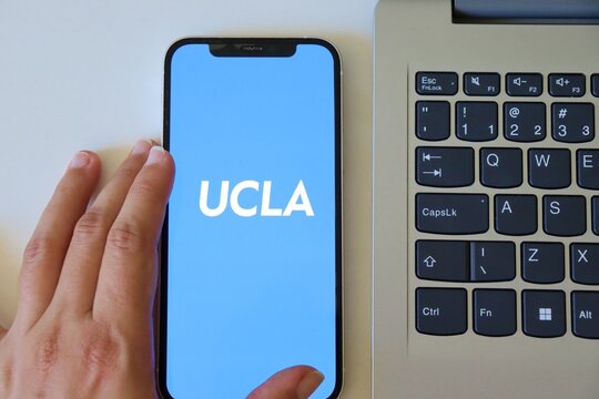 Salvador, Brazil - March 20, 2026: Close-up of a student's hand holding a smartphone displaying the UCLA (University of California, Los Angeles) official app logo. UCLA app.