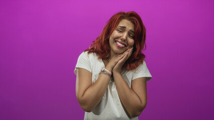 Fototapeta premium Young hispanic woman smiling with hands clasped to cheek in studio setting wearing white t shirt and watch; joy magenta.