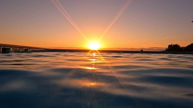 Stunning split underwater and above water view of a pool with the sun setting, showing the golden sunbeams and calm water
