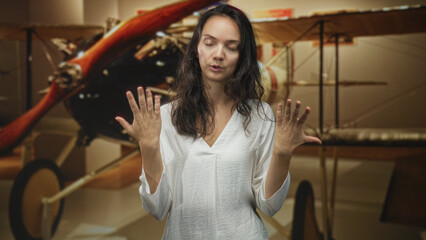 Woman covers face with hand and makes expressive hand gestures beside a vintage biplane propeller inside building  frustration reflection. © Krakenimages.com
