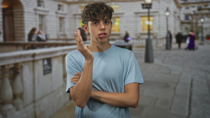 Fototapeta premium Teenage boy gestures with hands on a city street beside a stone balustrade, looking pensive and expressive; thoughtful reflection.