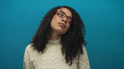 African american woman yawns with open mouth and red glasses wearing cream sweater in blue studio  fatigue. © Krakenimages.com