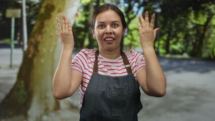 Woman with hands raised in a shrug gesture on a busy street by a large tree and red bus, wearing...