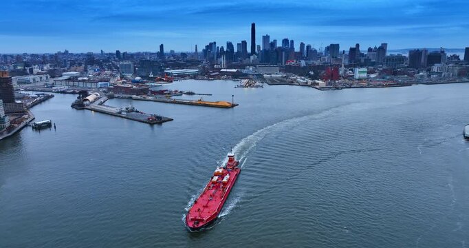 Tug boat pushes the oi tanker by the riverscape. New York skyline in the backdrop.