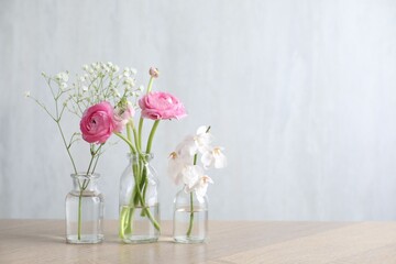 Fototapeta premium Beautiful flowers in vases on wooden table against light background. Space for text