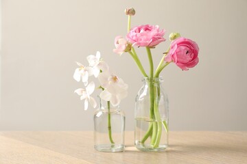 Obraz premium Different beautiful flowers in vases on wooden table against light background